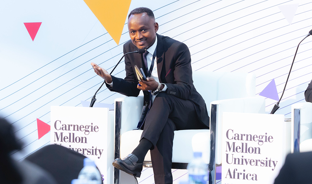 A man on stage leaning forward, smiling, and talking