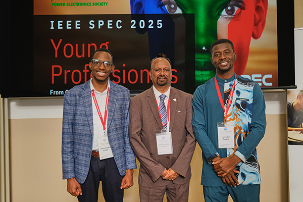 Three men in front of the banner for the conference