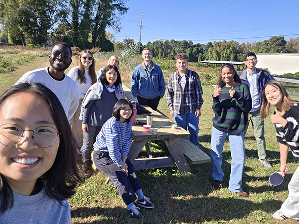 A group of smiling students who are outside around a picnic table