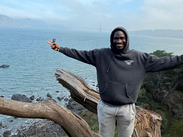 A man with arms spread wide. The ocean is visible behind him.