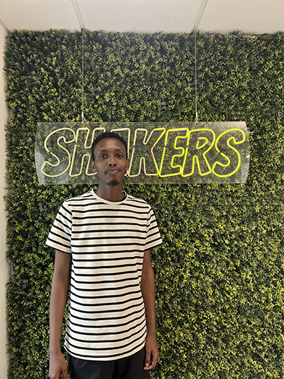 The student in front of a sign saying "Shakers"